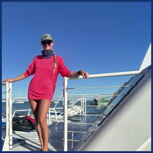Person in red shirt and cap on a boat deck with blue sky and railing.