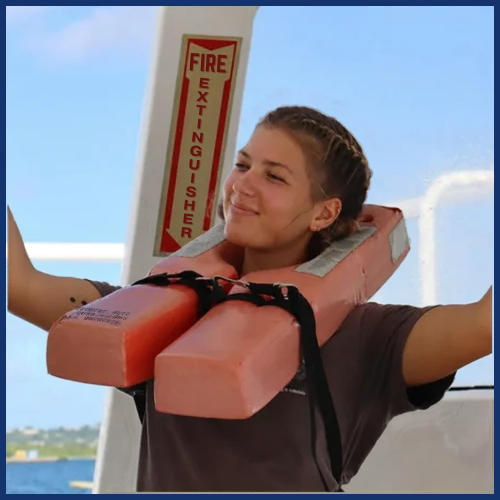 Person with a lifejacket smiling on a boat, fire extinguisher sign in background.