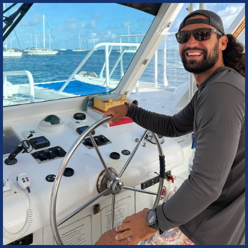 Man with sunglasses smiling while steering a boat.