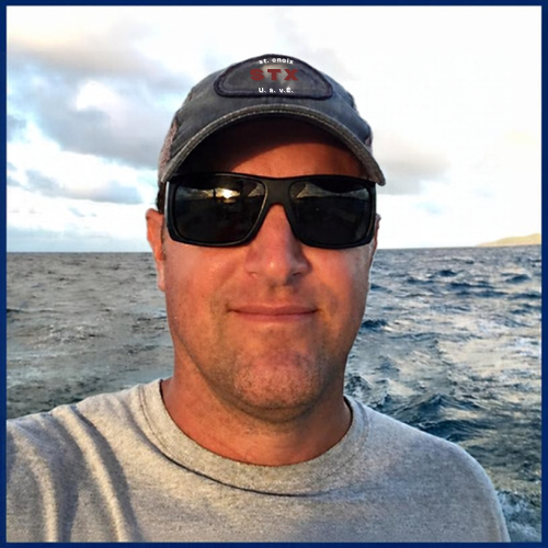 Man wearing sunglasses and cap smiling by the ocean.